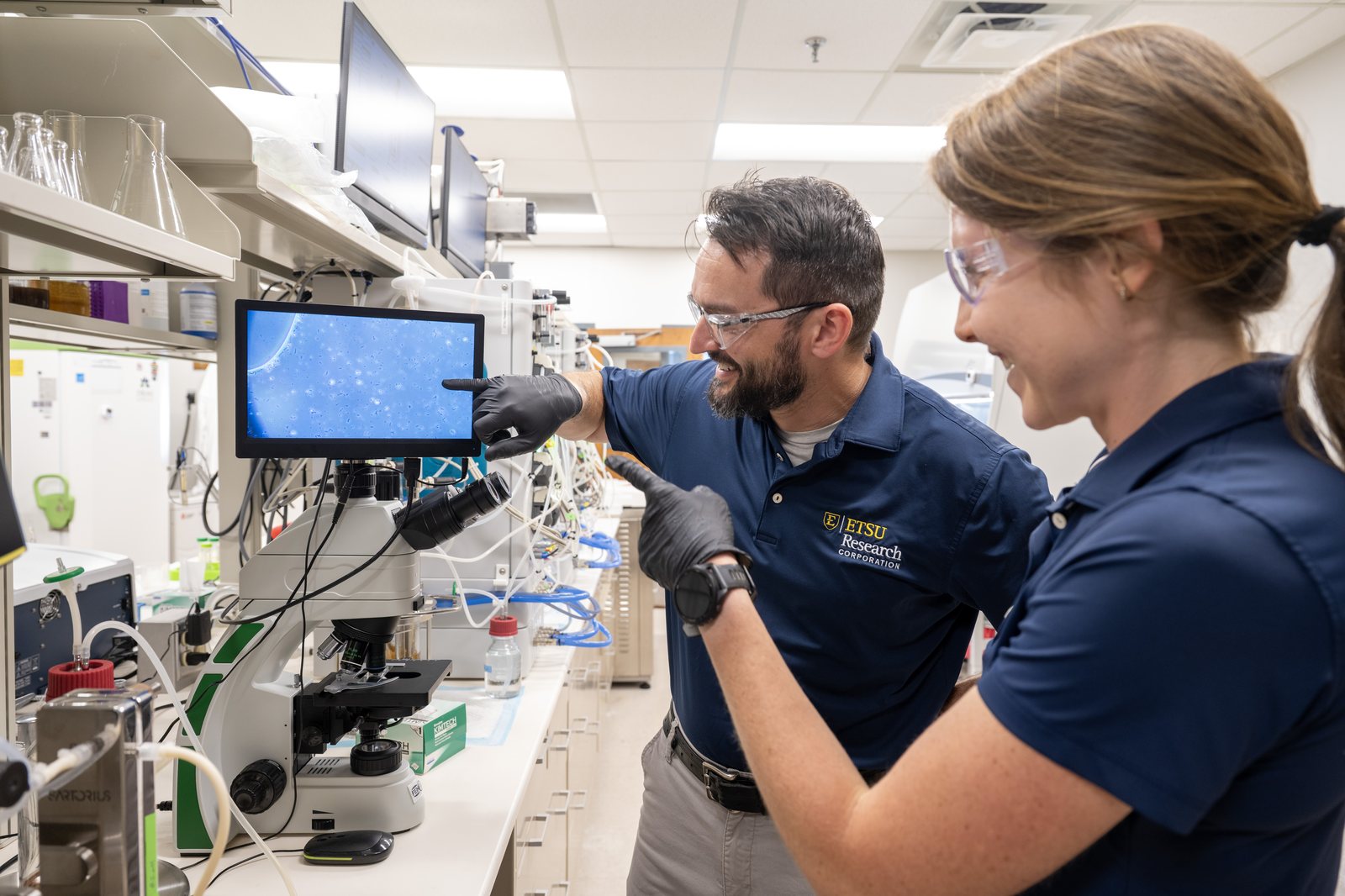 ETSU Research Corporation scientists reviewing cell cultures on a microscope display in the Valleybrook biomanufacturing lab