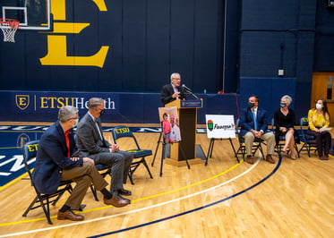 Doc Sander speaks at a podium in Brooks Gym during a press conference announcing Finengan's Challenge. Ballad Health and ETSU officials are to his sides.