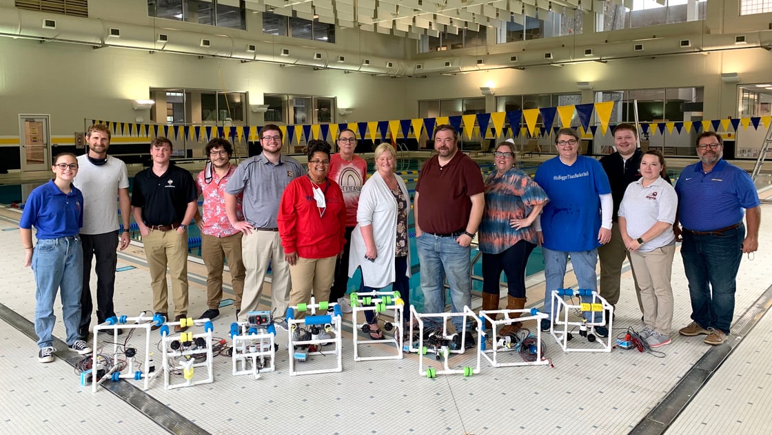 Thirteen people stand and pose in front of the ETSU pool with remote operated vehicle robots. 