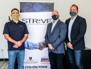 Three men in masks stand beside a Strive poster.