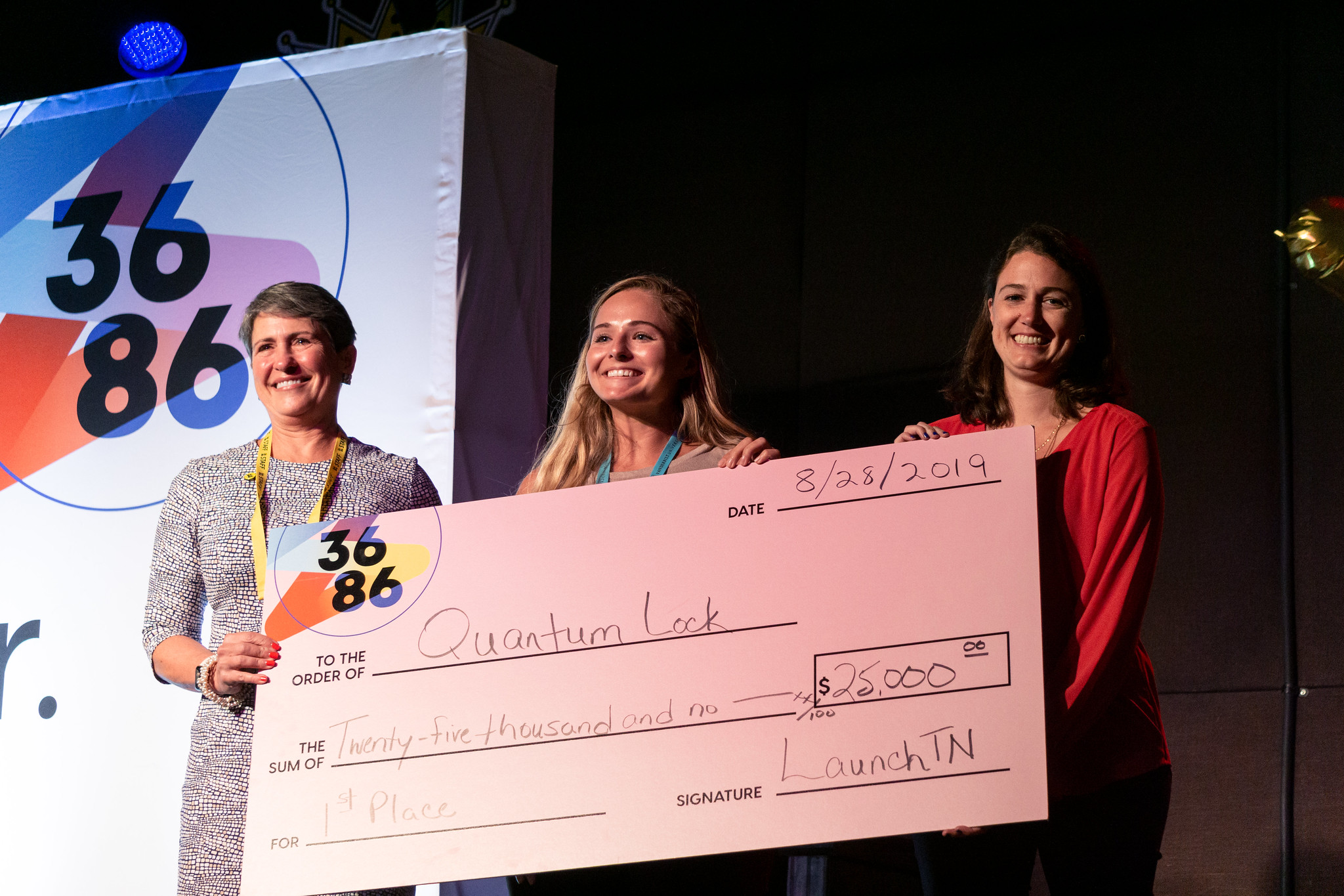 Three women hold a large check for Quantum Lock. The check is signed by Launch Tennessee.